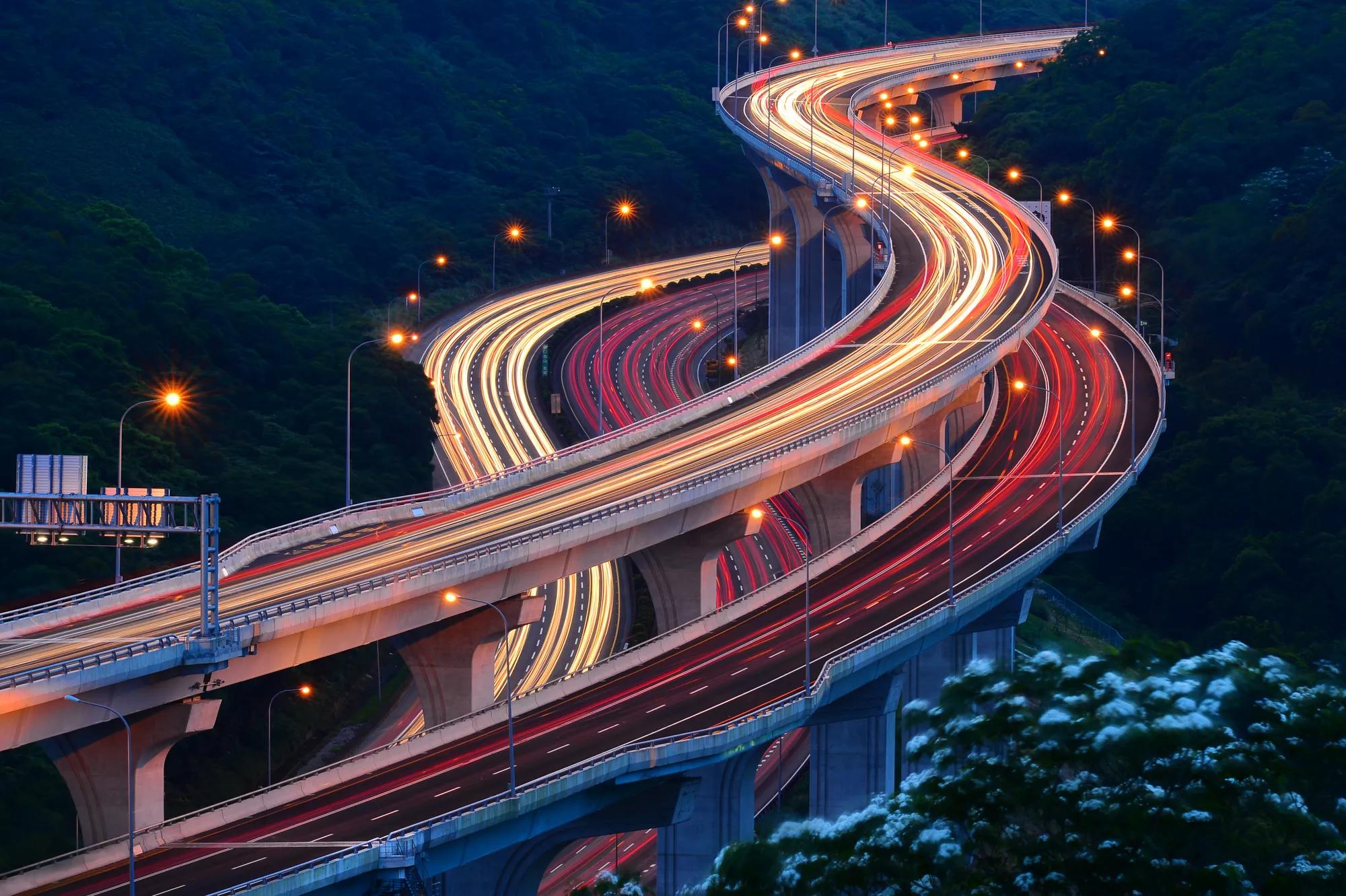Three winding highway overpasses and underpasses at night with the traffic lights in motion