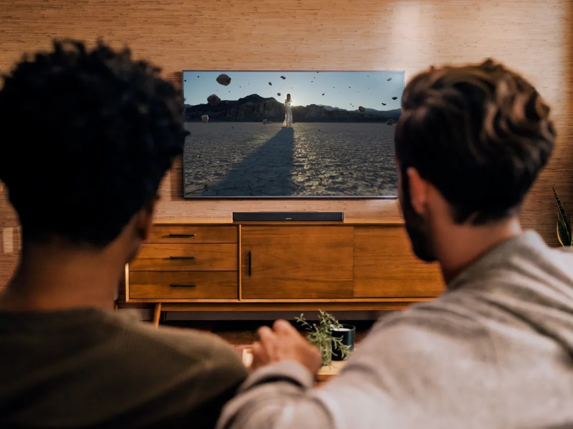 Friends watching TV with a Bose Smart Soundbar on a TV console.