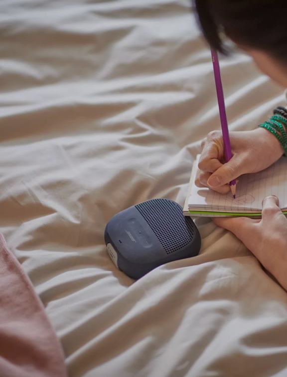 Jeune femme étendue sur son lit et écoutant de la musique avec une enceinte Bluetooth SoundLink Micro 