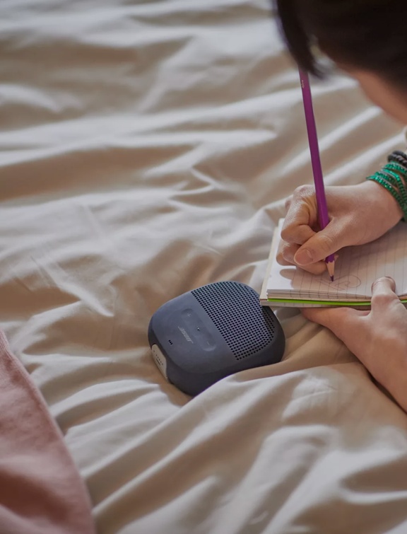 Young woman listening to music from a SoundLink Micro Bluetooth Speaker while lying on her bed