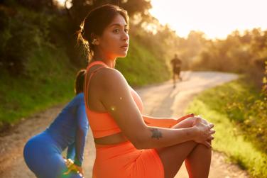 Une femme portant des écouteurs oreilles libres Bose Ultra en train de faire des étirements avant d’aller courir