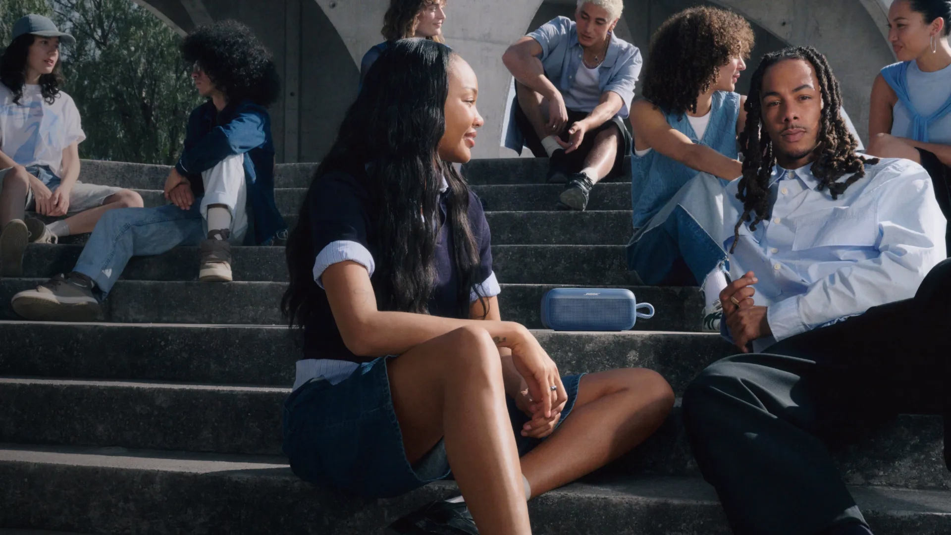 Des amis qui &eacute;coutent une enceinte portative Bose SoundLink Plus assis dans les marches d&rsquo;un escalier.