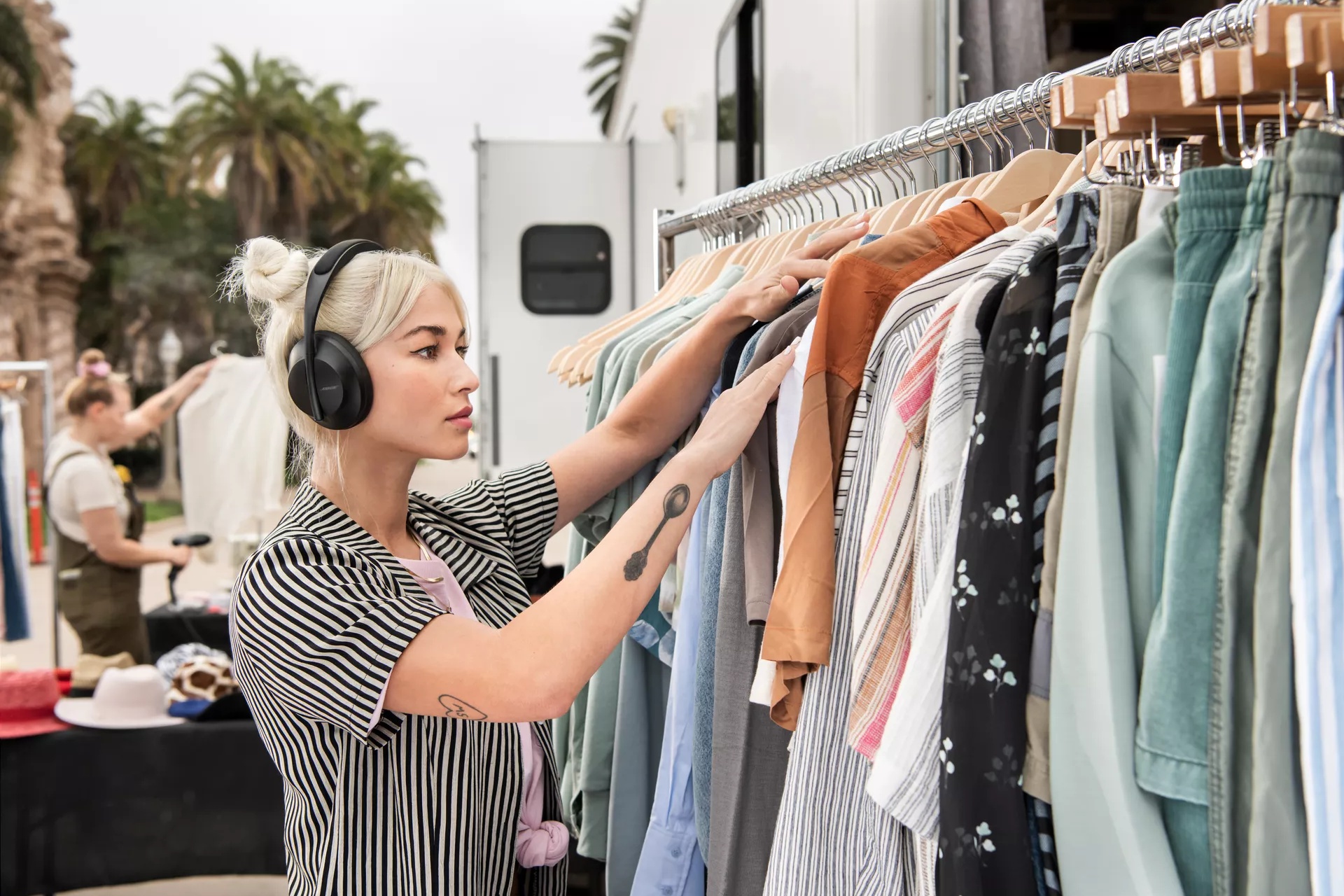Woman wearing Bose Noise Cancelling Headphones 700 while selecting an outfit from a clothing rack