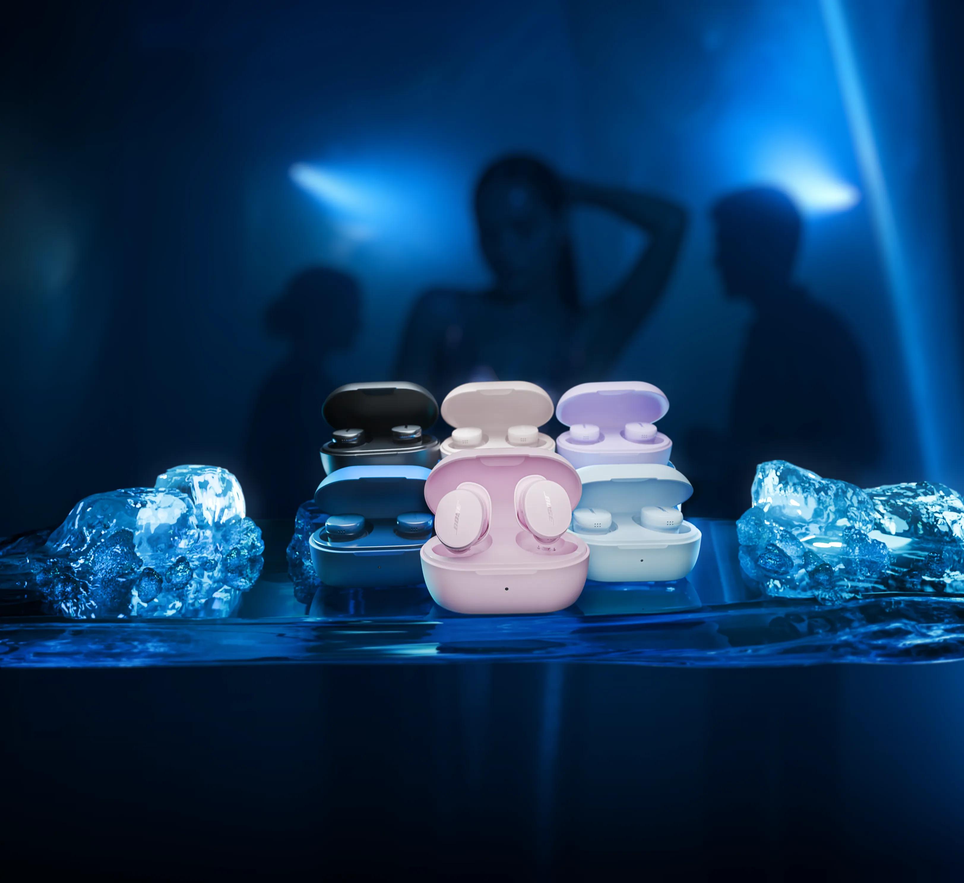 Bose QuietComfort Earbuds in a variety of colors on a table with ice and people dancing in the background.