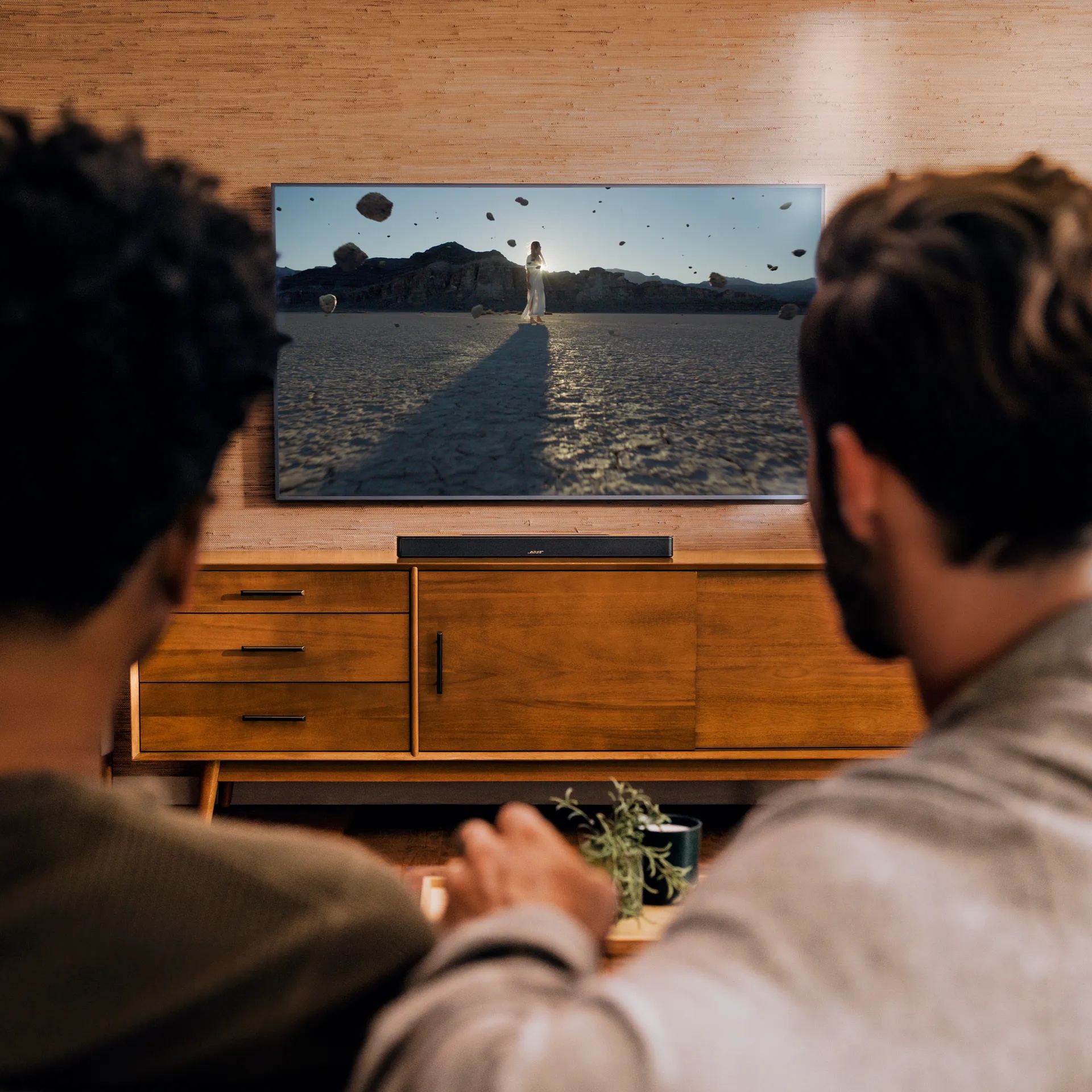 Friends watching TV with a Bose Smart Soundbar on a TV console.