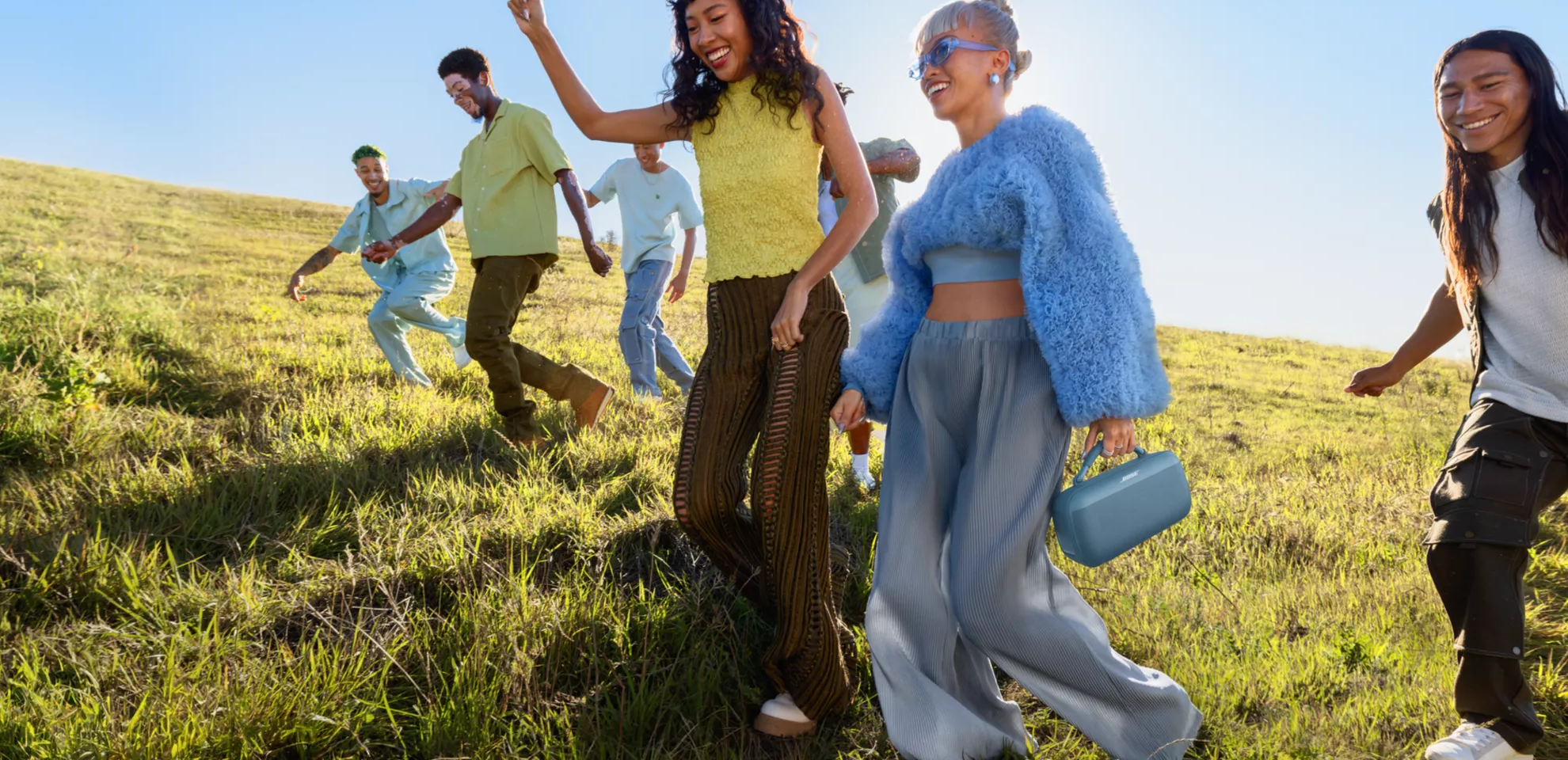 Young people walking through a field carrying a Bose SoundLink Max Portable Speaker