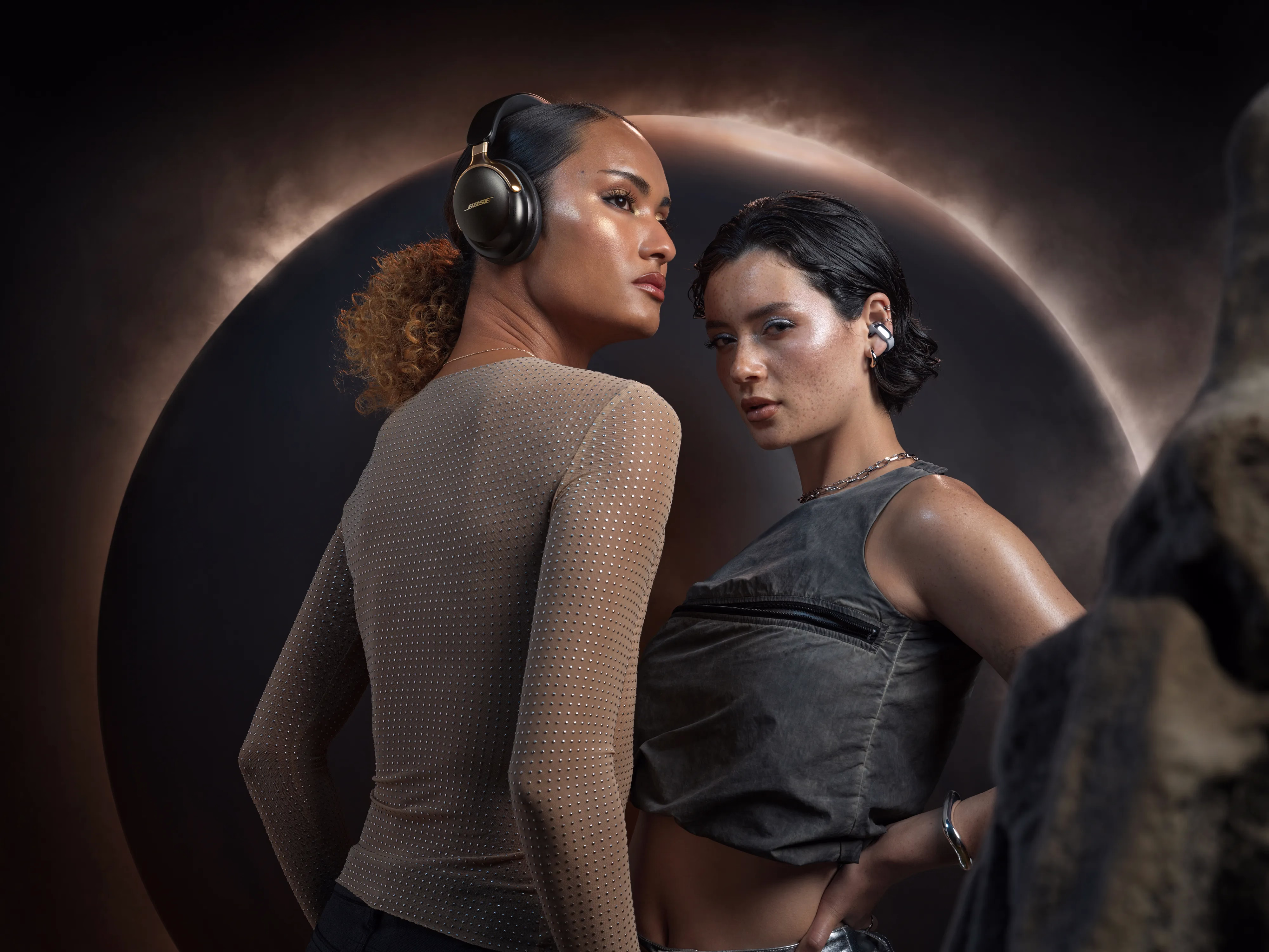Two women posing against a dramatic backdrop, one wearing QuietComfort Ultra Headphones LE (2nd Gen) and the other wearing Ultra Open Earbuds LE.