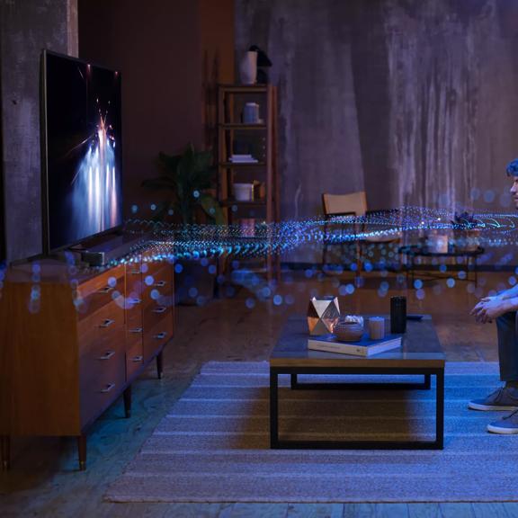 Homme dans un salon regardant la télévision avec des ondes sonores rayonnant du système d’enceintes montrant les effets du Dolby Atmos