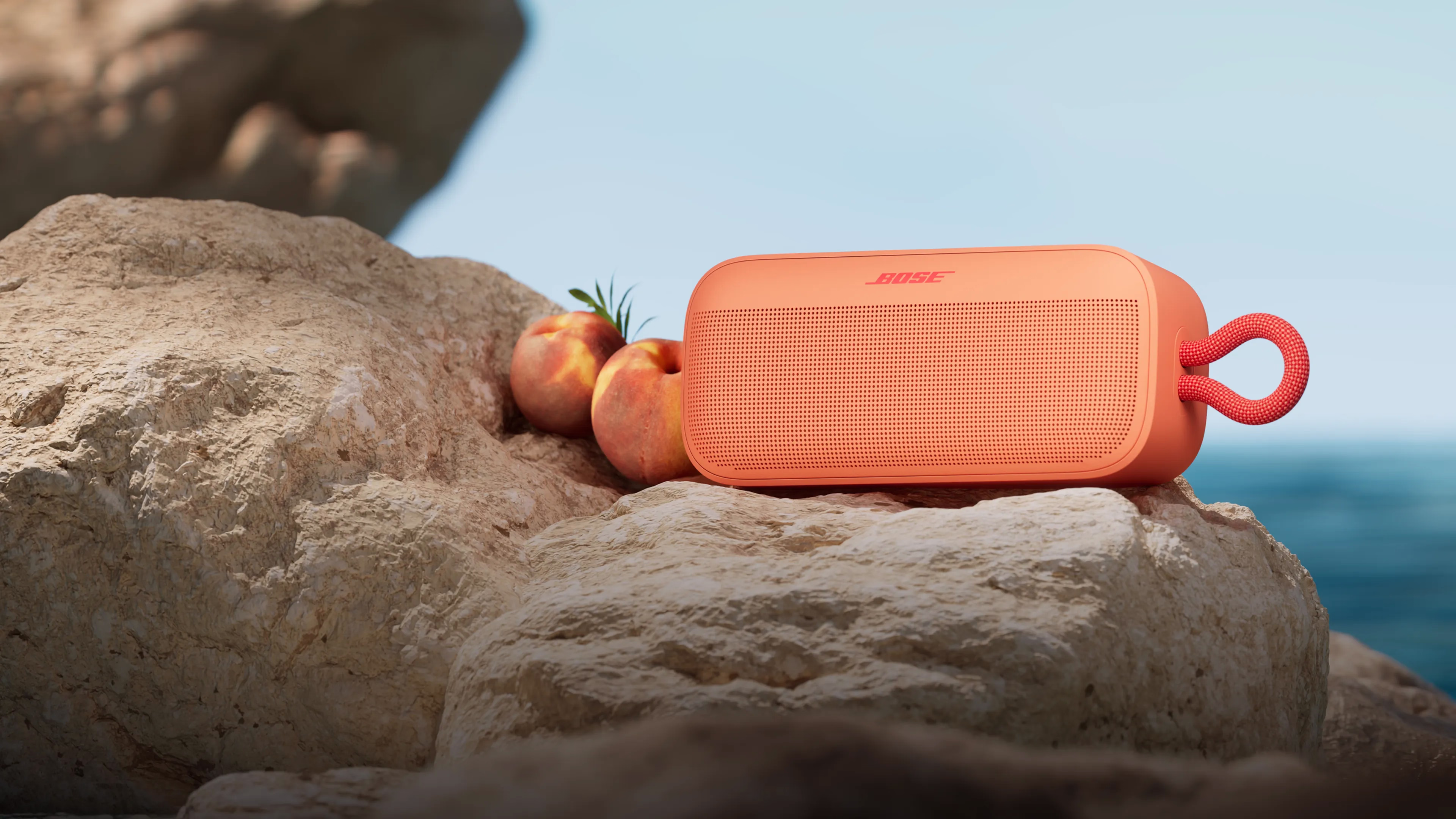 A peach leaning against a Sunset Peach SoundLink Plus Portable Speaker on a beach.