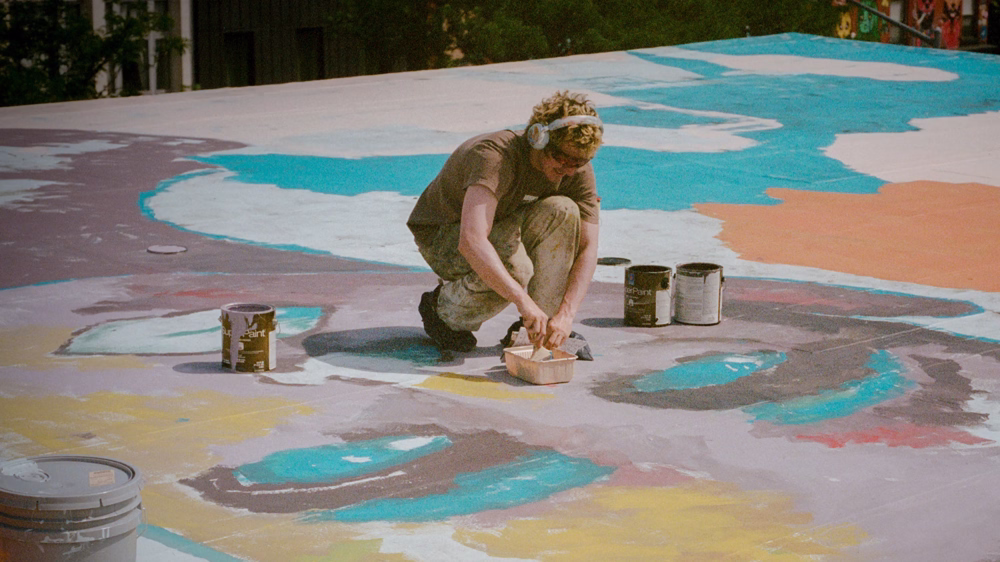 KidSuper hand painting the rooftop of a city building.