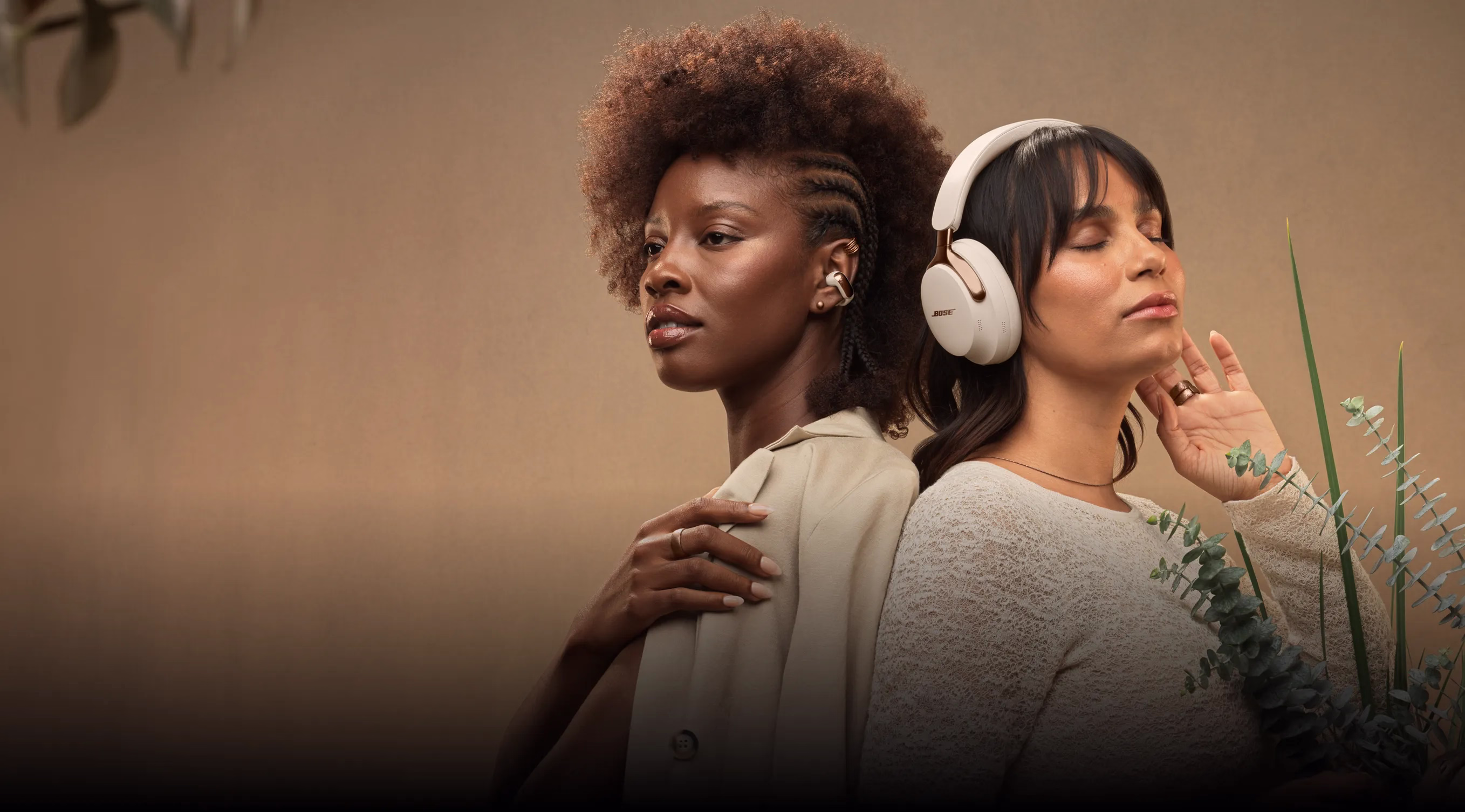 Two women standing back-to-back. One wearing Bose Ultra Open Earbuds, the other wearing QuietComfort Ultra Headphones (2nd Gen).