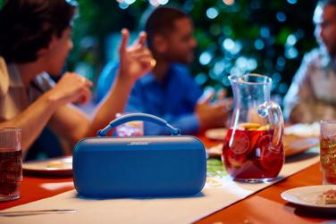 Bose SoundLink Max Portable Speaker playing music on a table at an outdoor barbecue