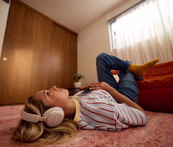 Woman laying down on a living room floor wearing Bose QuietComfort Ultra Headphones (2nd Gen).