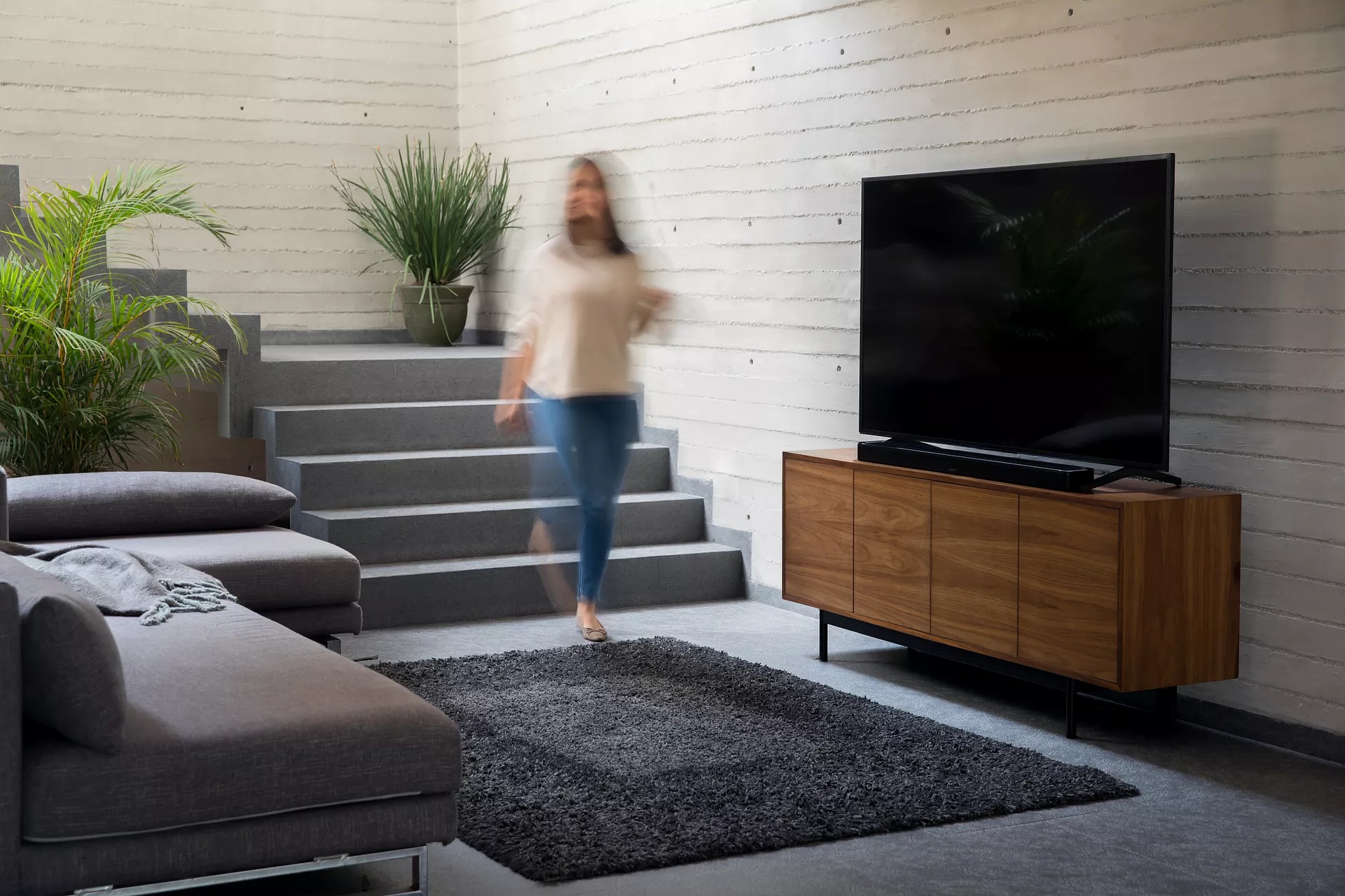 Woman walking downstairs into living room as music plays from a Bose Soundbar