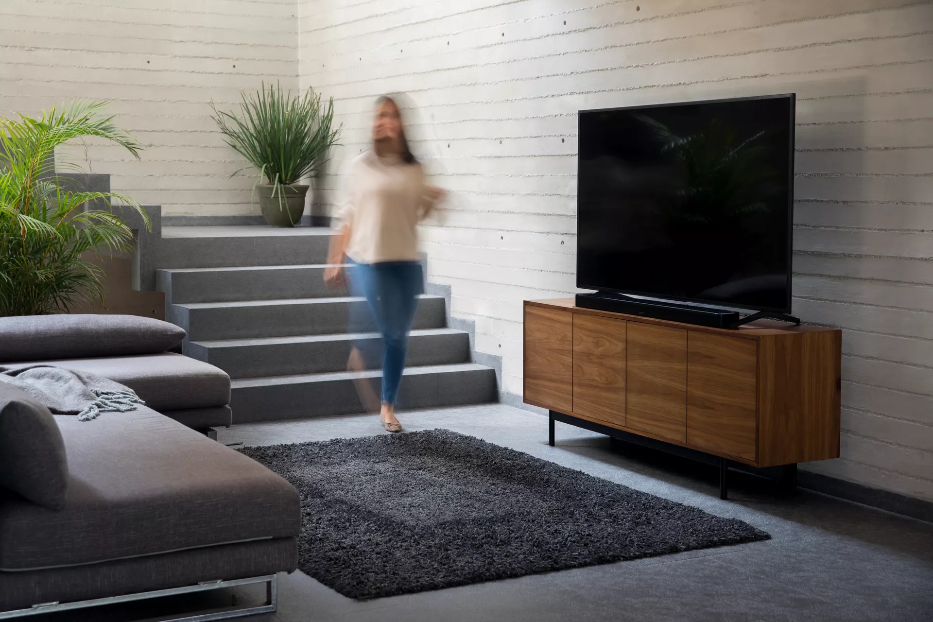 Woman walking downstairs into living as music plays from a Bose Soundbar