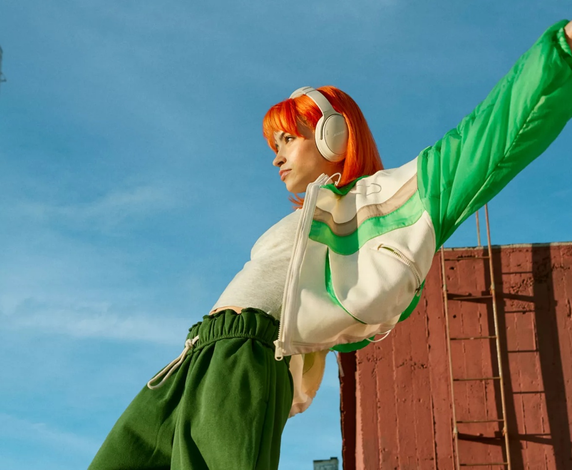 Girl with orange hair and green jacket dancing to music with QuietComfort Headphones