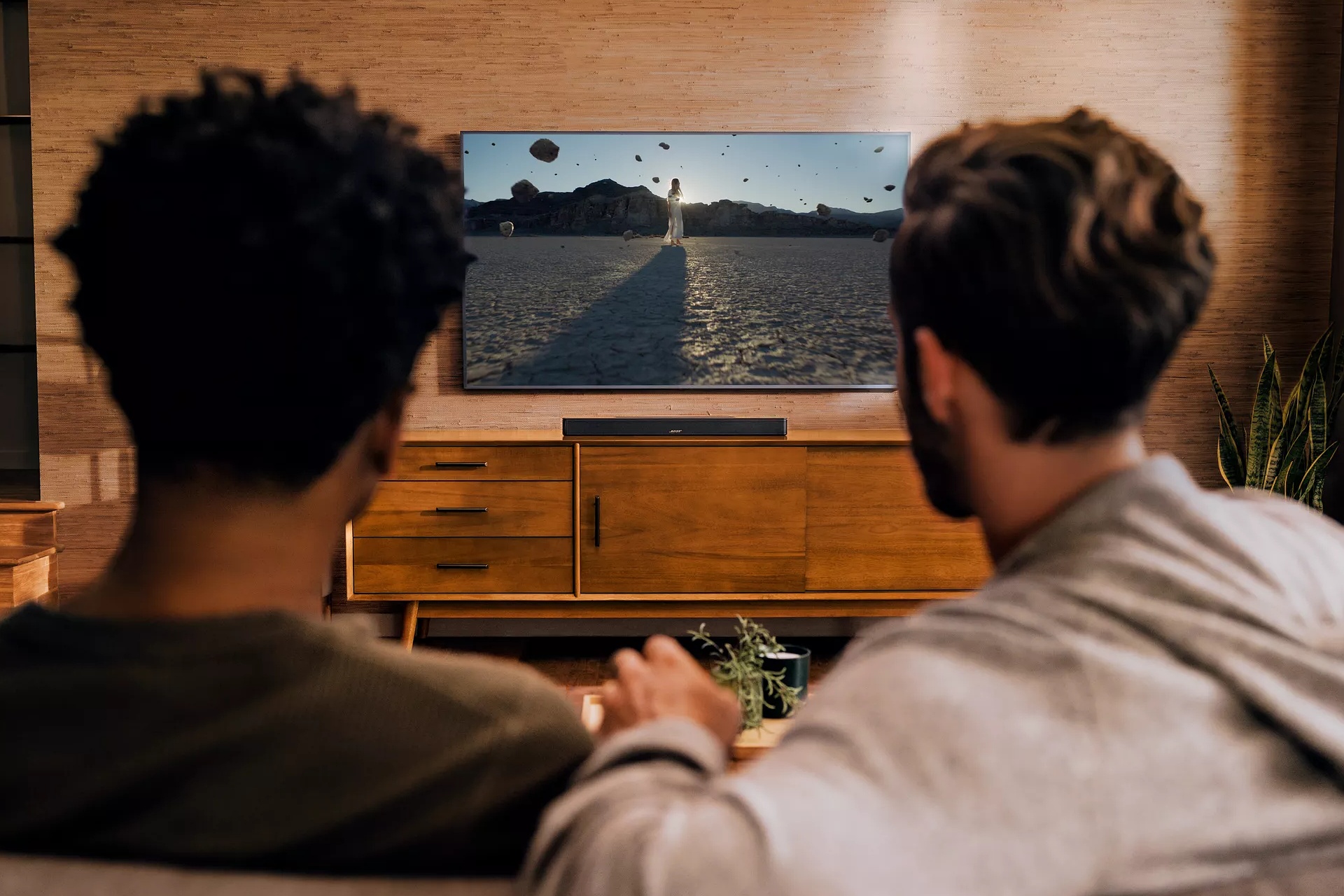 Two guys sitting on couch, watching a movie, and experience Dolby Atmos through a Bose Soundbar