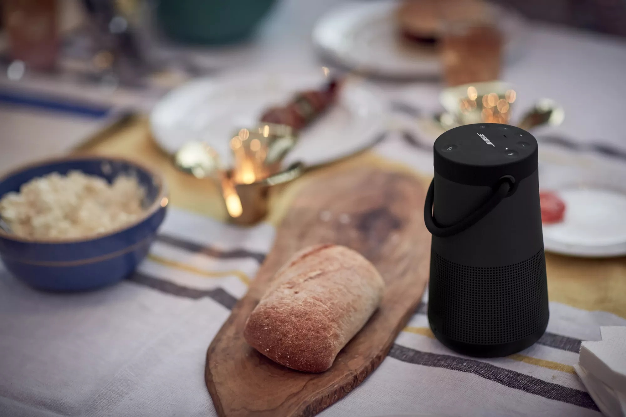 Une enceinte SoundLink Revolve+ II active sur une table extérieure sur laquelle est disposée de la nourriture